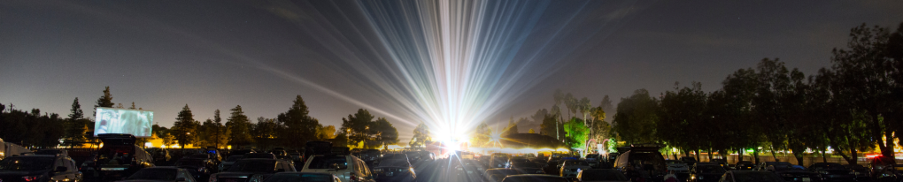 image ooking back from screen to the projector. Beams of light shine towards the viewer. Cars are parked